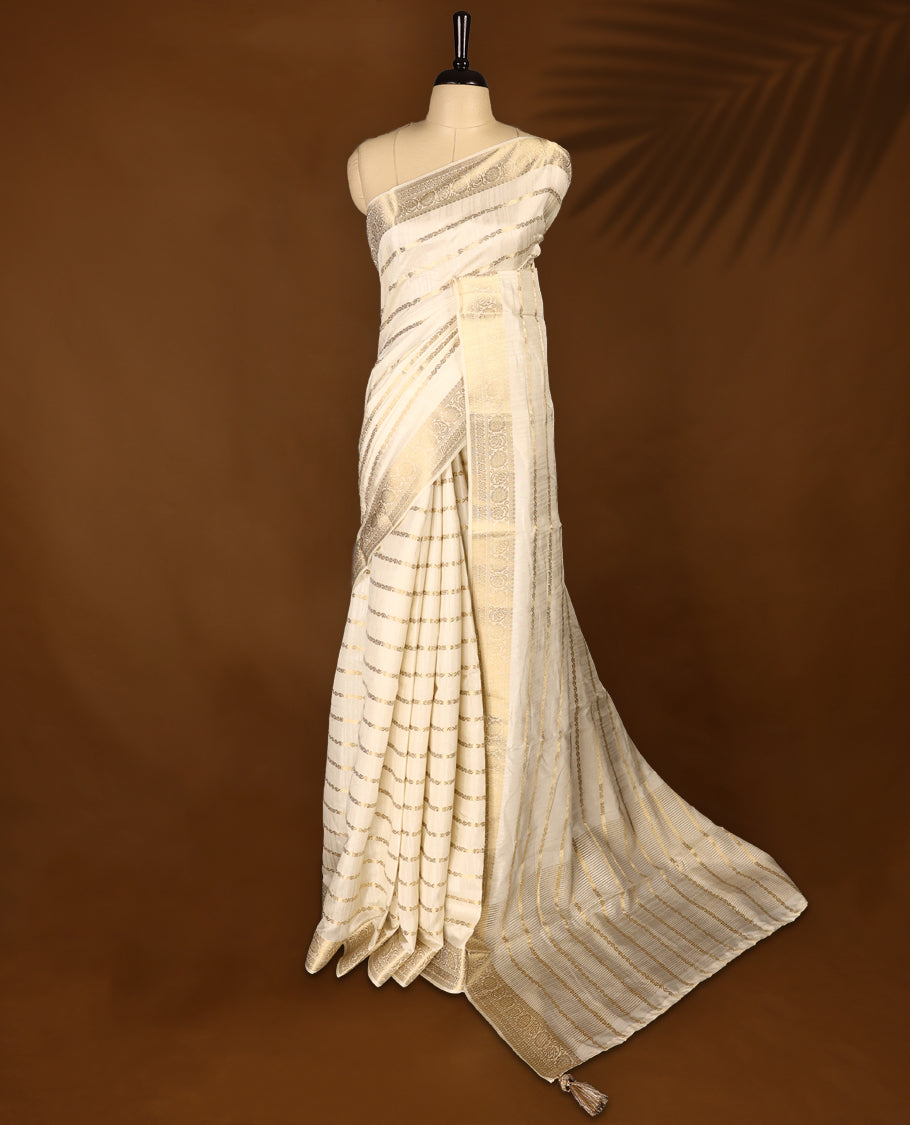 Elegant Off White colour Tussar Kerala saree featuring a Floral Kodi Stripes across body, muted gold zari banarasi Style border, and a striking Gold Zari woven Bold pallu, paired with a matching blouse.