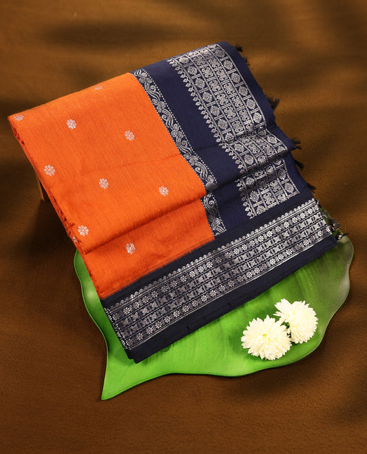 Deep Orange colour mixed Kalyani cotton saree featuring Silver zari flower motifs throughout the body, paired with Deep Navy Blue colour traditional border and pallu, with matching blouse