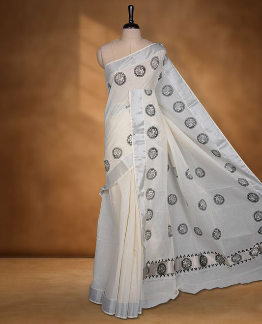 Off-white colour cotton Kerala saree featuring a subtle silver kasavu border, adorned with classic black cirlcle peacock motifs across the body and pallu, and paired with a matching blouse.