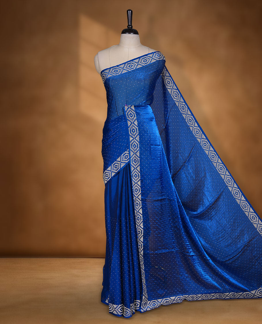 Royal Blue colour chiffon designer saree, featuring delicate scattered stone detailing all over the body, highlighted with intricate stone work and a heavy geometric stone pattern along the border and pallu, paired with a matching embellished blouse.a