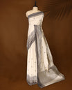 Cream colour Soft Tussar saree adorned with intricate grey woven buttas across the body, complemented by an ornate grey border featuring traditional motifs, and finished with a striped pallu, paired with a matching blouse.