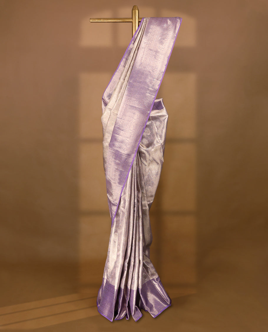 Pastel lavender Colour Kancheepuram tissue silk saree embellished with intricate silver zari work on the body, elegantly enhanced by a lavender traditional Chakkram and floral kodi design border, and paired with a matching blouse.