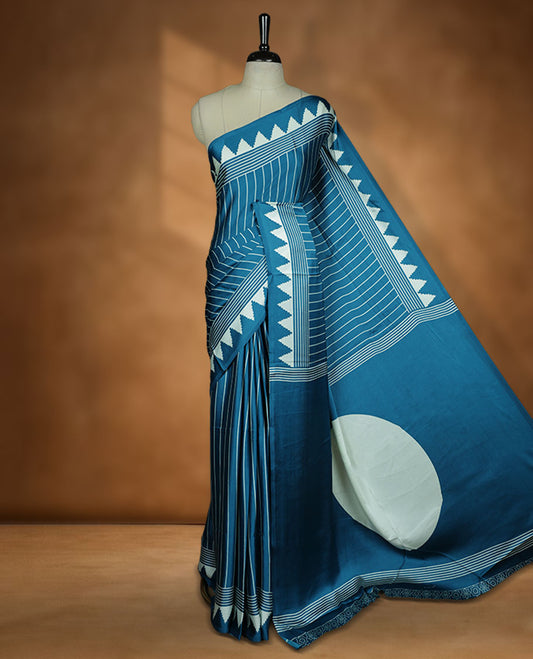 Teal Blue colour semi modal saree featuring bold white geometric borders and fine stripe detailing, finished with an oversized white circular motif on the pallu, paired with a matching printed blouse.