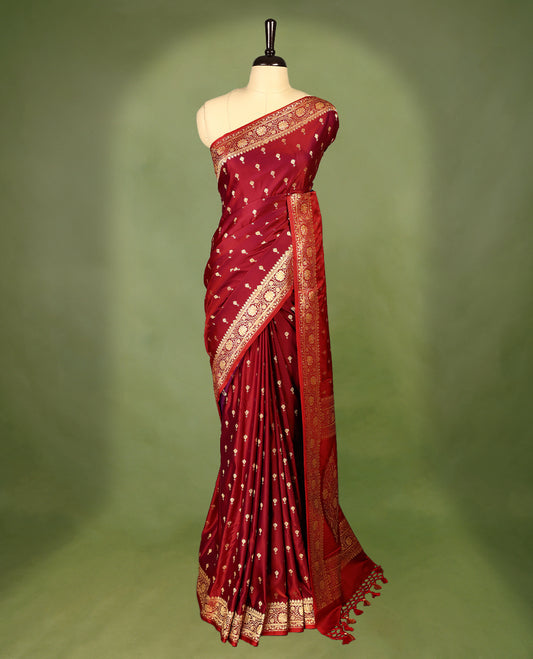 Deep red colour semi Banaras satin crepe saree featuring gold zari woven flower motifs across the body, complemented by an intricately designed traditional banarasi border and richly woven pallu, paired with a matching blouse piece.