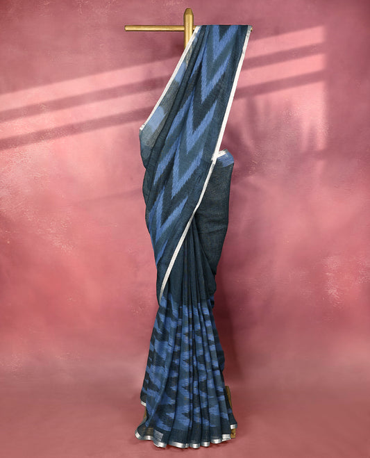 Blue and black colour pure linen saree featuring subtle ikkat style patterns all over the body, paired with a simple silver border and comes with a matching blouse