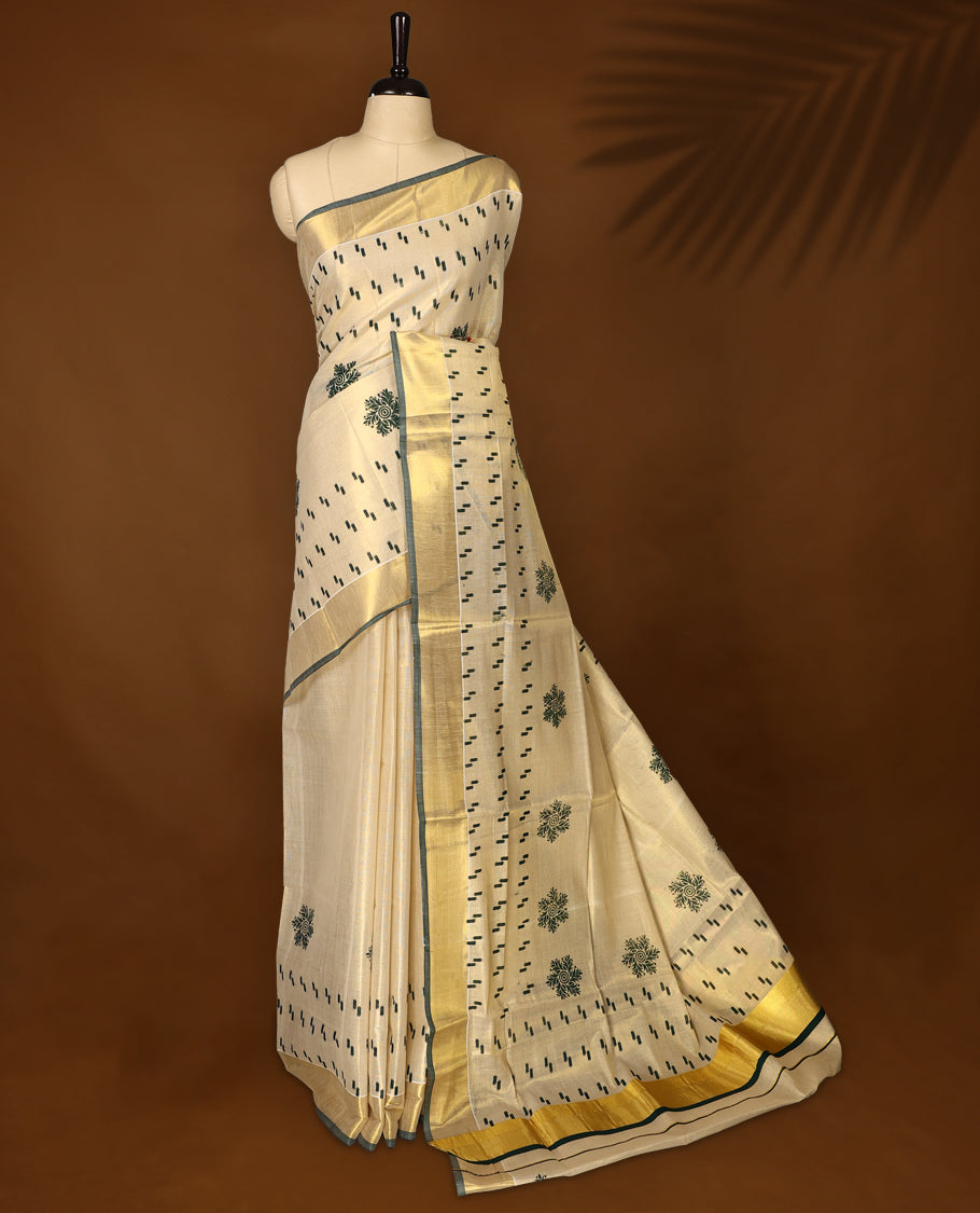 Elegant off white tissue Kerala saree with green woven motifs and floral buttas, paired with a rich golden zari border and pallu paired with matching blouse.