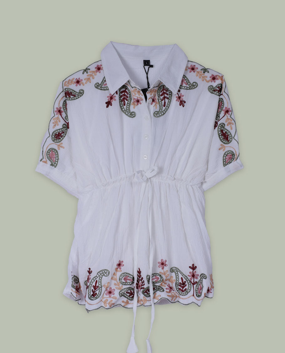 White short tunic top with collared neckline, short sleeves, multicolour paisley and floral embroidery on shoulders and hem, and a drawstring waist with long tasseled ties.