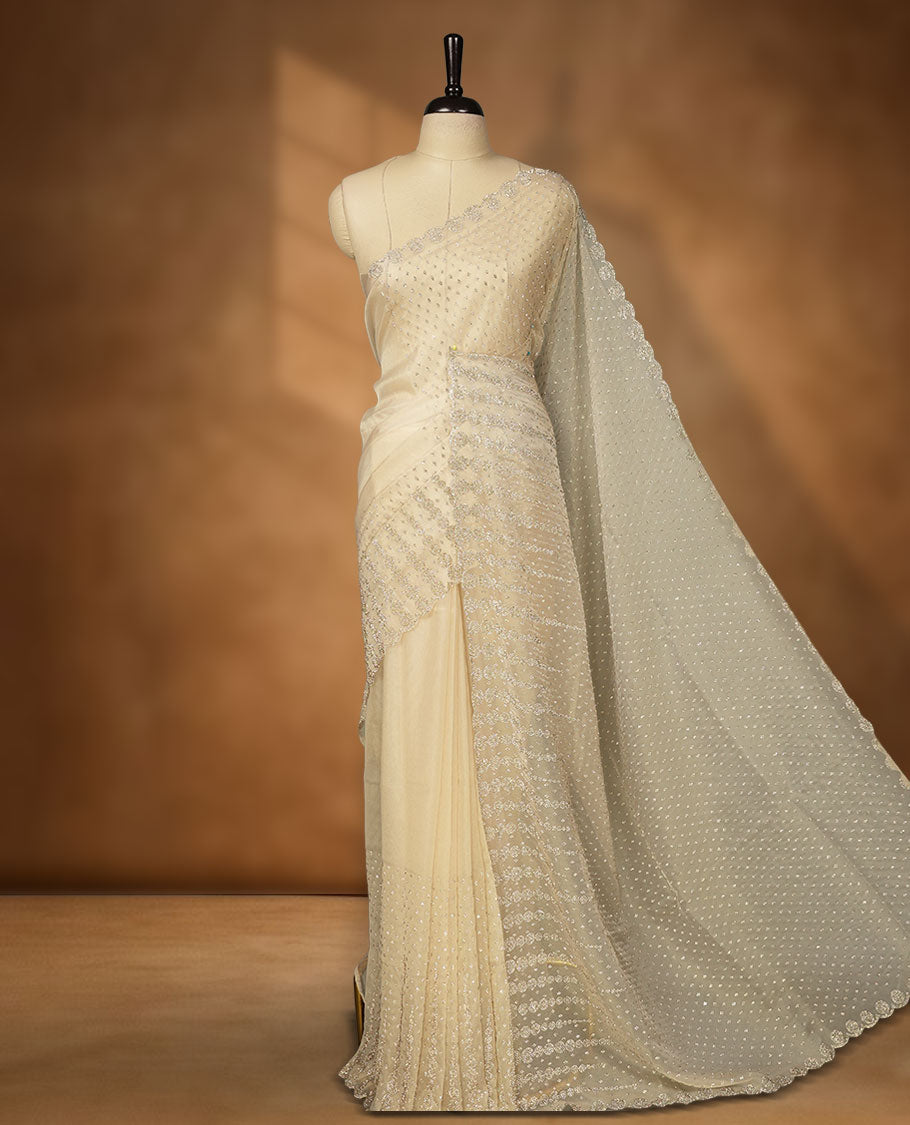 Beige colour net shimmer fancy saree adorned with gold stone buttas all over the body, paired with a delicate stone worked border, with matching blouse