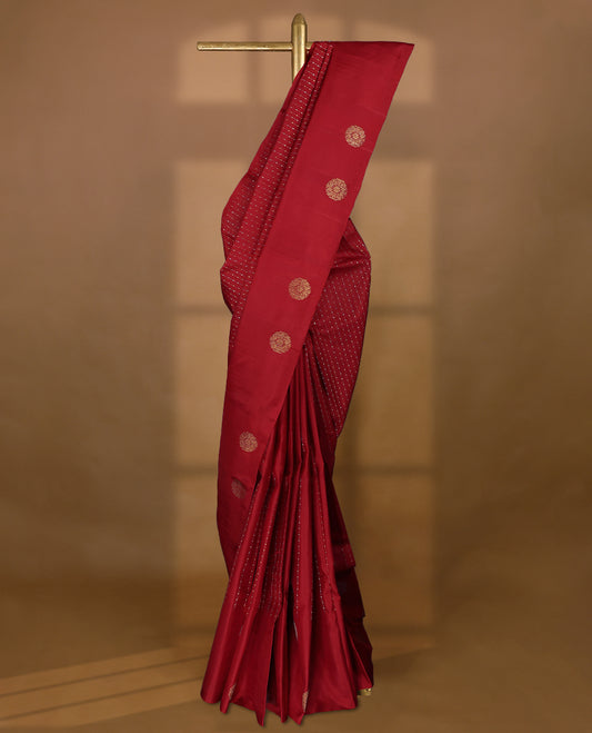 Deep red colour traditional Kancheepuram silk saree adorned with vertical rows of small golden motifs on the body, featuring a self-coloured simple border with floral chakra motifs, and paired with a matching blouse.