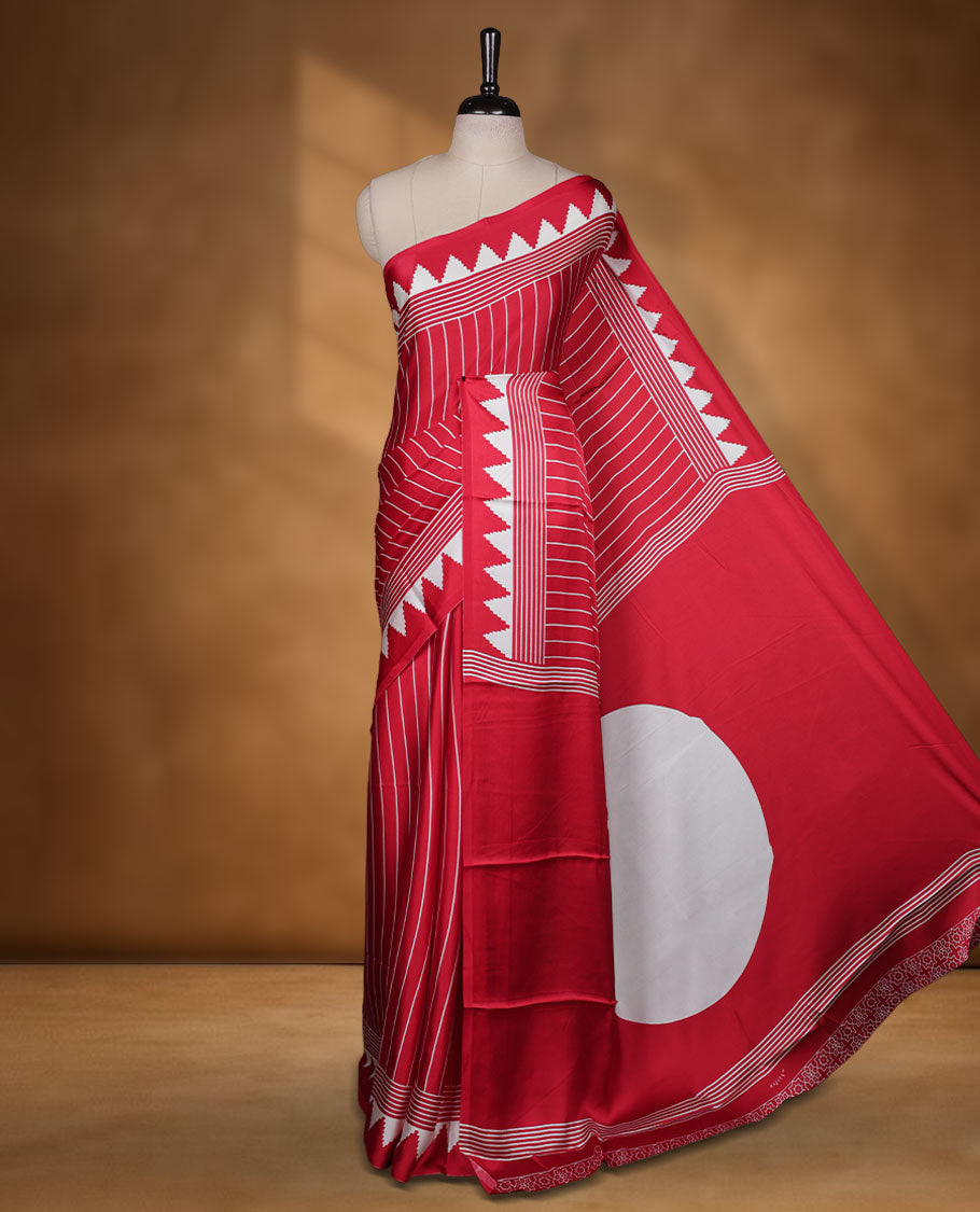 Red colour semi modal saree featuring white colour geometric borders and fine stripe detailing, finished with an oversized circular motif on the pallu, paired with a matching printed blouse.