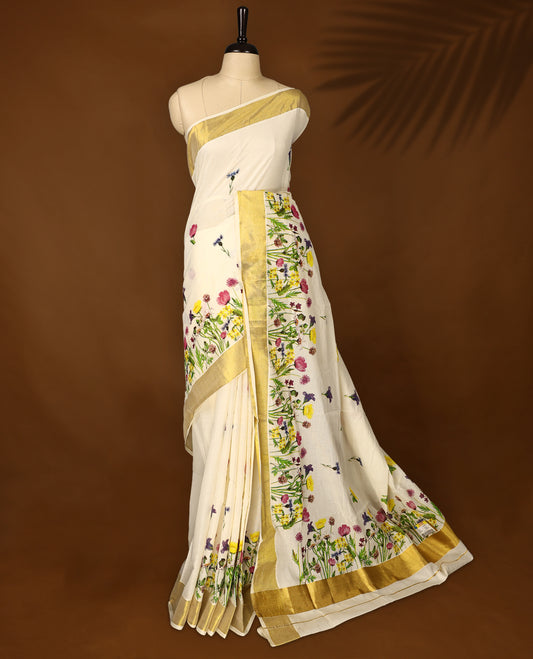 Elegant off white colour cotton Kerala saree with vibrant floral prints and a rich golden zari border, paired with a matching blouse. Perfect for festive occasions and day events with a graceful, natural charm.