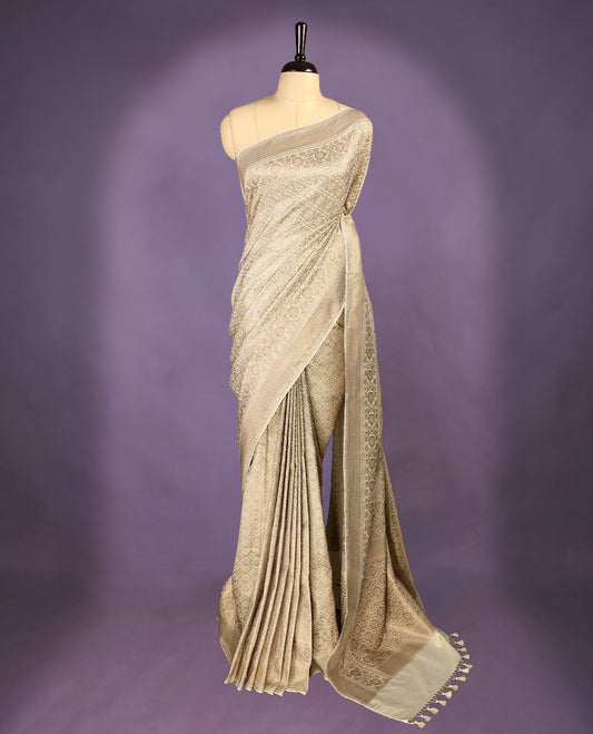 Off White colour semi Banaras Katan saree featuring an antique Gold zari jacquard body, complemented by a self colour traditional border with a floral kodi design, paired with a matching blouse