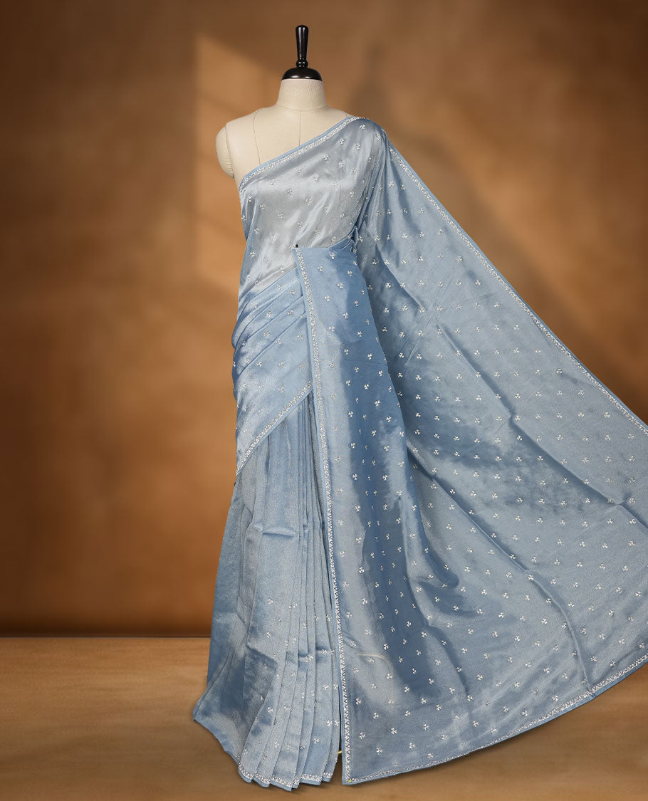 Pastel Blue colour net shimmer fancy saree adorned with scattered white stone buttas all over the body, paired with a delicate stone worked border and matching blouse featuring floral vine stone embroidery
