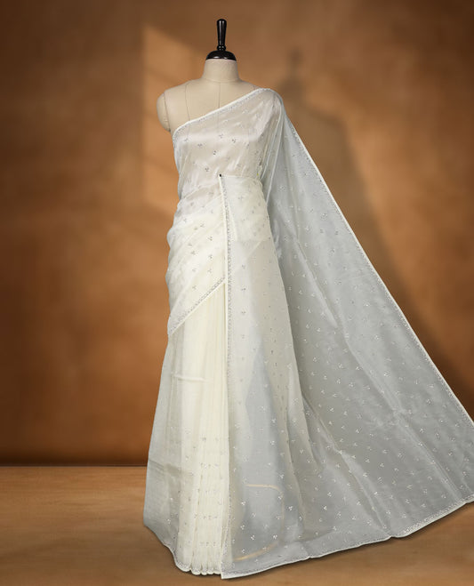 Off white Colour net shimmer fancy saree adorned with scattered white stone buttas all over the body, paired with a delicate stone worked border and matching blouse featuring floral vine stone embroidery