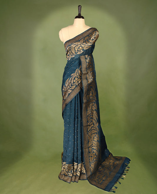 Deep teal colour Tussar Banaras saree adorned with delicate golden zari motifs on the body, rich floral woven zari border and grand pallu, paired with a matching blouse for an elegant and regal traditional look.