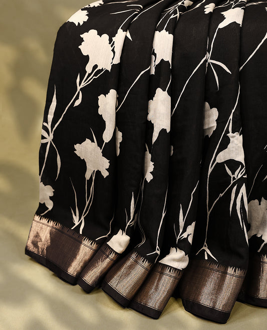 Black colour viscose semi printed saree adorned with a golden zari border, featuring elegant white floral prints across the body, and comes with a matching blouse