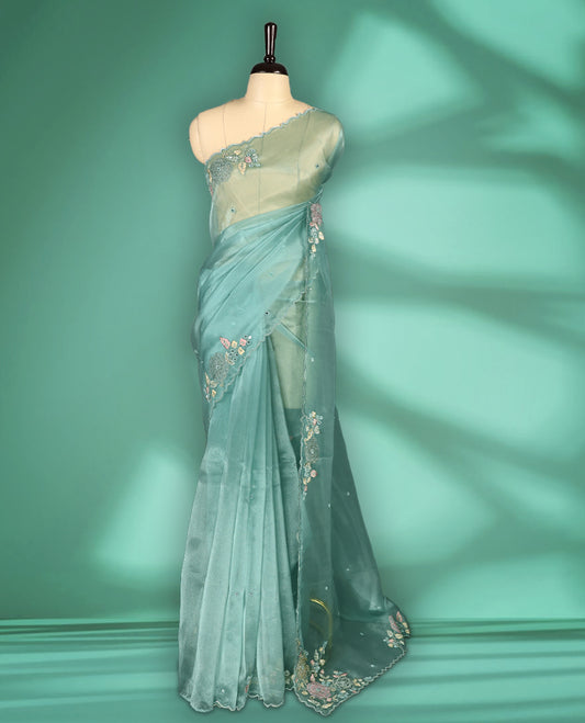 Light Blue Colour organza saree featuring delicate floral embroidery with applique, bead, mirror, and thread detailing on the body and scalloped border, lending a soft feminine charm, paired with a matching blouse.