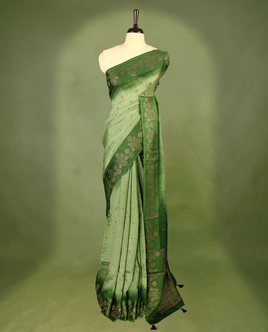 Green double shade semi Banaras Tussar Georgette saree adorned with elegant antique gold zari floral motifs across the body, featuring a detailed woven border and grand pallu, paired with a matching blouse piece.