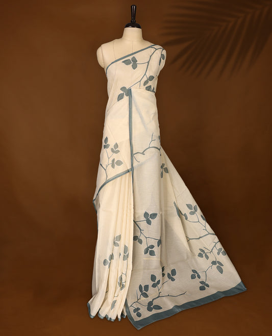 Cream colour Tussar cotton Kota saree featuring elegant stone blue leafy branch motifs across the body, accentuated with a subtle stone blue border, and paired with a matching blouse for a graceful and minimal look.