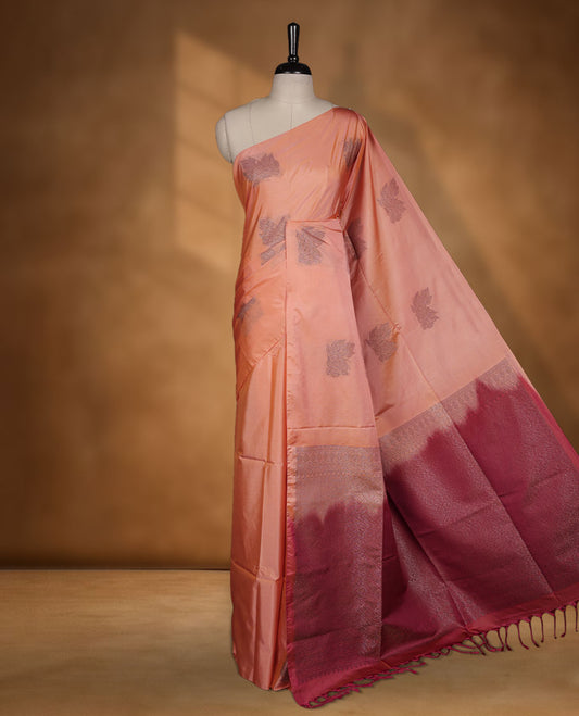 Dark peach colour semi soft silk saree adorned with delicate woven floral motifs on the body, complemented by a contrast red colour woven pallu with intricate detailing and tassel accents without border & Comes with a matching blouse piece.