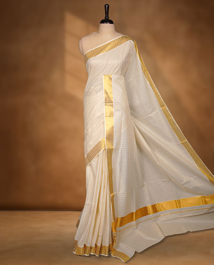 Off-white colour cotton Kerala saree featuring a subtle gold checkered weave, highlighted with a classic rich gold kasavu border along the edges and pallu, and paired with a matching blouse perfectly blending traditional charm with understated elegance.