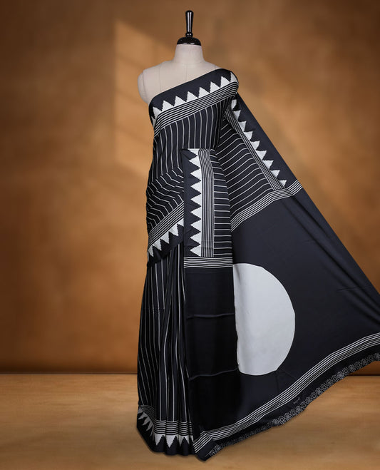 Black colour semi modal saree featuring white colour geometric borders and fine stripe detailing, finished with an oversized circular motif on the pallu, paired with a matching printed blouse.