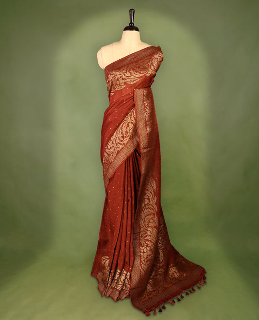 Rust Orange colour Tussar Banaras saree adorned with delicate golden zari motifs on the body, rich floral woven zari border and grand pallu, paired with a matching blouse for an elegant and regal traditional look.
