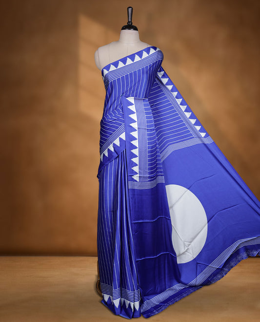 Royal blue colour semi modal saree featuring white colour geometric borders and fine stripe detailing, finished with an oversized circular motif on the pallu, paired with a matching printed blouse.