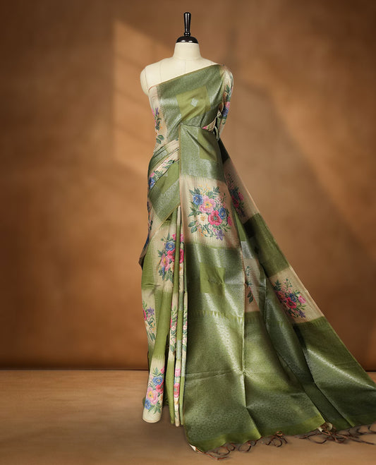 Green color semi tussar Banarasi saree featuring vibrant multi-color floral prints across the body, with shimmering geometric zari patterns, and a matching blouse detailed with silver woven buttas.