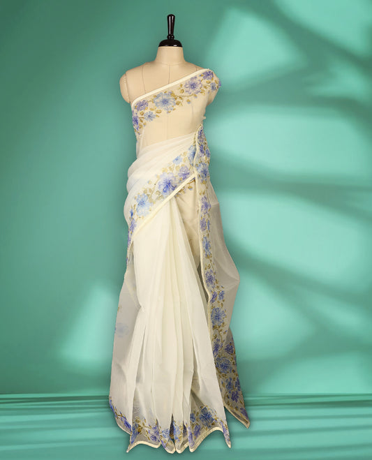 Ivory white colour organza saree adorned with blue floral print with thread detailing on the border and pallu, in a sheer finish that adds elegance, paired with a matching blouse for a graceful look.