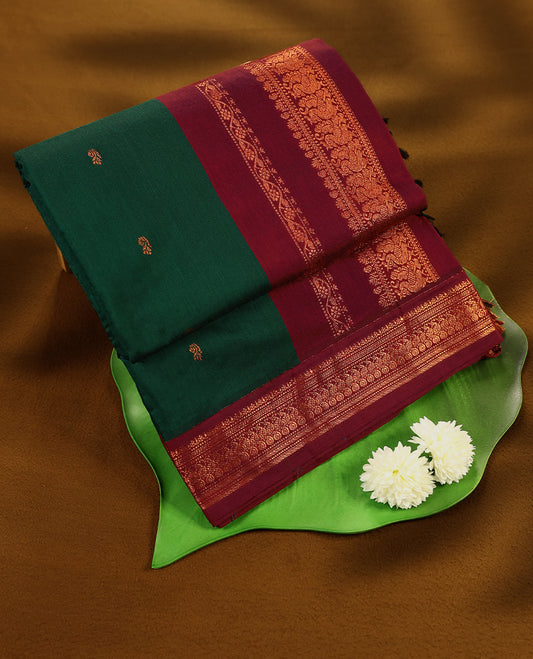 Bottle Green colour mixed Kalyani cotton saree featuring Copper zari Mango motifs throughout the body, paired with a Maroon colour traditional border and pallu, with matching blouse