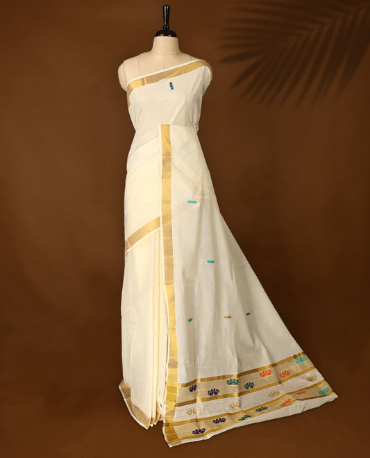 Elegant off white colour cotton Kerala saree featuring a golden zari border, colorful thread buttas, and vibrant peacock motifs on the pallu, and paired with matching blouse.