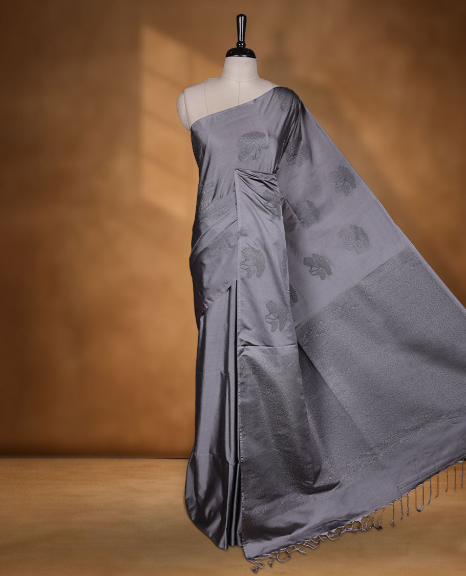 Silver gray colour semi soft silk saree adorned with delicate woven floral kodi motifs on the body, complemented by a Self colour woven pallu with intricate detailing and tassel accents without border & Comes with a matching blouse piece.