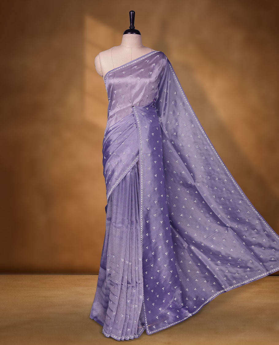 Lavender colour net shimmer fancy saree adorned with scattered white stone buttas all over the body, paired with a delicate stone worked border and matching blouse featuring floral vine stone embroidery