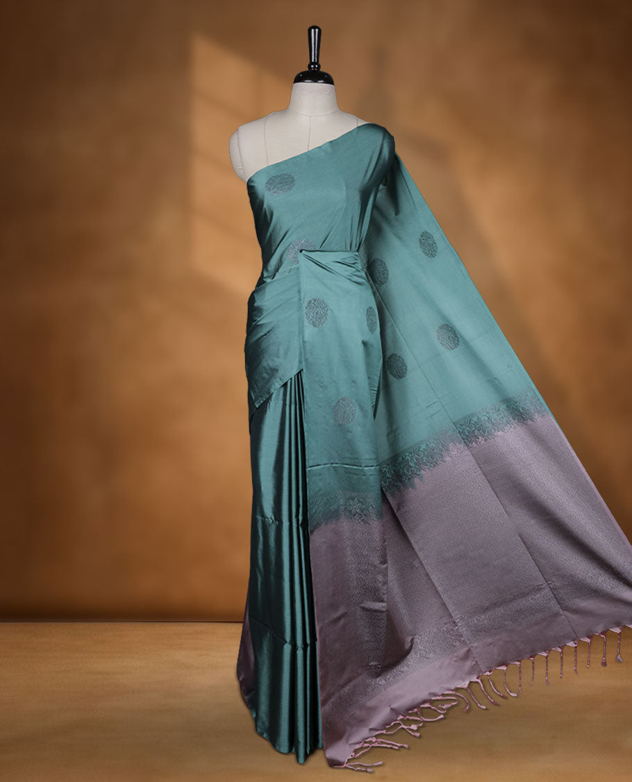 Pine green colour semi soft silk saree adorned with delicate woven floral motifs on the body, complemented by a contrast dusty pink colour woven pallu with intricate detailing and tassel accents without border & Comes with a matching blouse piece.