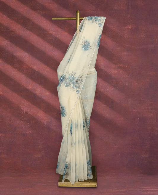 White colour pure organza saree featuring blue Colour floral prints with intricate bead and sequin work across the body, adorned with a matching embellished border, complemented by a worked pallu and paired with a heavily worked matching blouse.