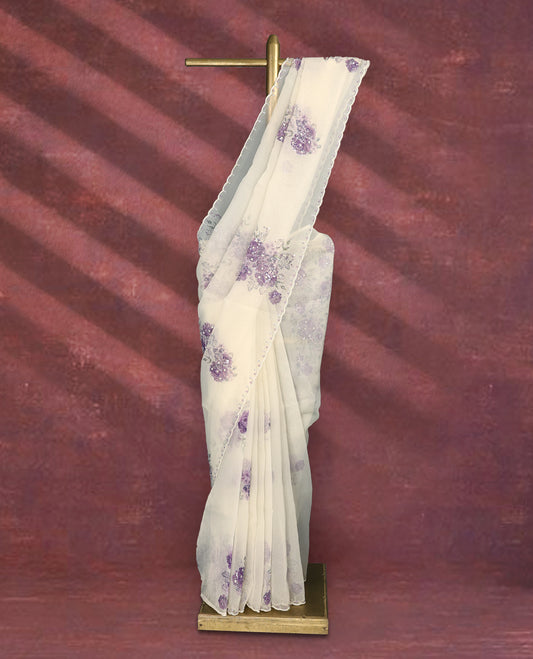 White colour pure organza saree featuring purple Colour floral prints with intricate bead and sequin work across the body, adorned with a matching embellished border, complemented by a worked pallu and paired with a heavily worked matching blouse.