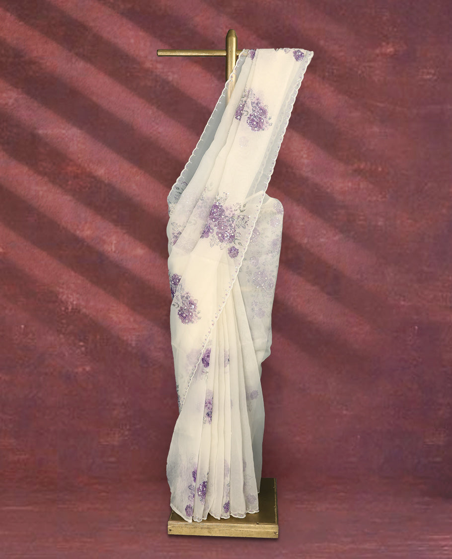 White colour pure organza saree featuring purple Colour floral prints with intricate bead and sequin work across the body, adorned with a matching embellished border, complemented by a worked pallu and paired with a heavily worked matching blouse.