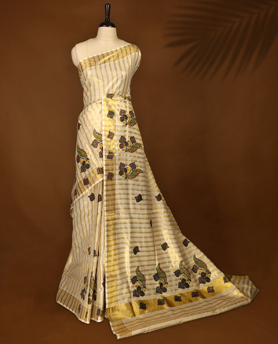 Elegant off white colour tissue Kerala saree featuring golden zari stripes, adorned with vibrant multicolour paisley motifs, and finished with a shimmering gold border and pallu & Paired with a matching blouse.