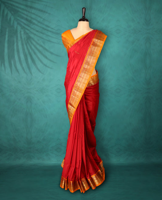 Deep Red colour Traditional Kancheepuram Silk saree with small gold motifs on body, orange colour traditional border with intricate gold zari weaving, grand zari pallu, perfect for Bharatanatyam, with matching blouse.