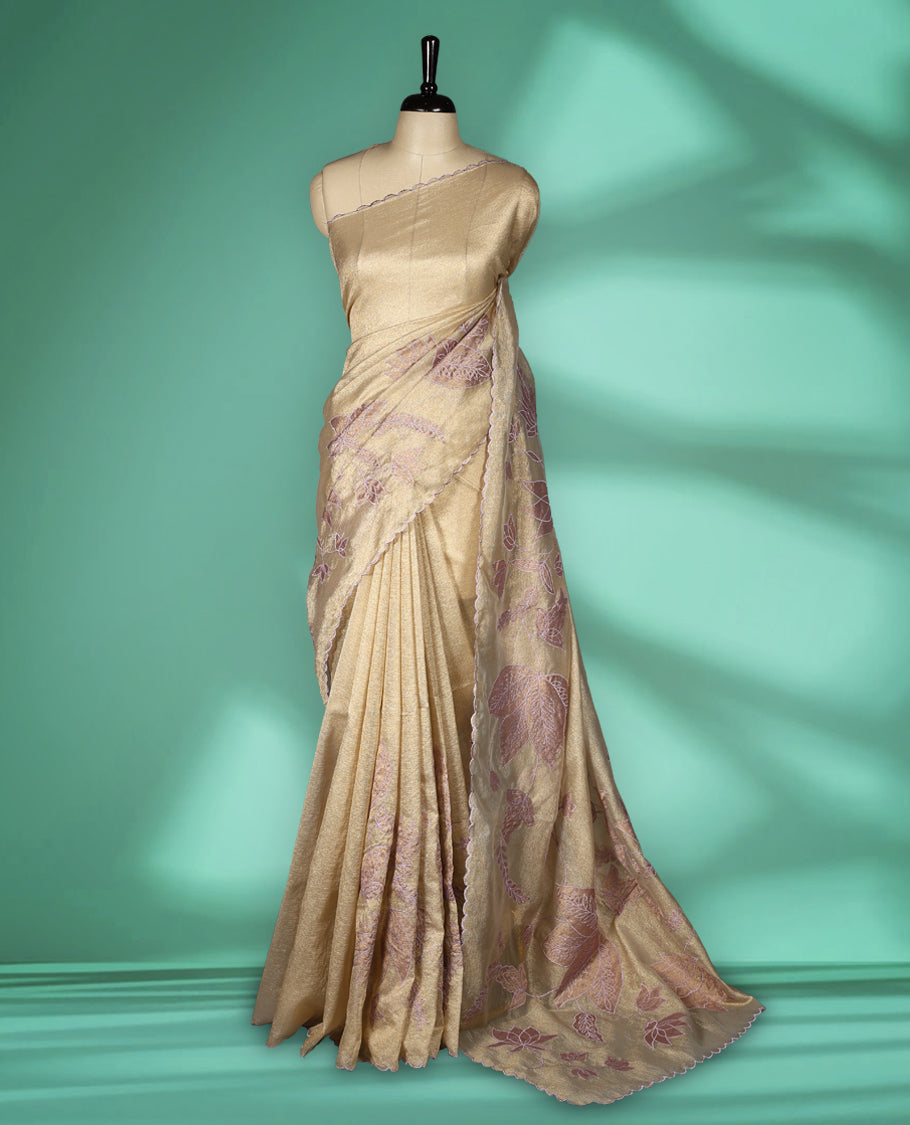 Champagne beige colour organza designer saree featuring subtle woven texture on the body, adorned with soft mauve floral embroidery along the border and pallu, finished with scalloped Thread edging paired with matching blouse.