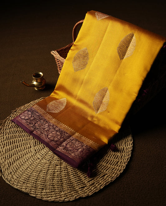 Golden Yellow Colour Banaras Soft Silk Saree with Gold Zari Oval Textured Buttas, Simple Decorative Pallu Border, Grand Pallu with Ornate Circular and Foliate Motifs in Maroon and Gold Tones, and Matching Deep Maroon Blouse.