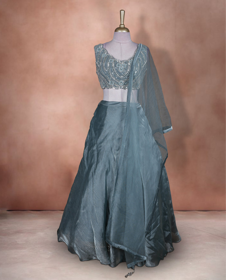 Dusty teal blue colour lehenga set with stitched sleeveless heavily embellished blouse featuring scalloped neckline, matching stitched flared lehenga, and plain sheer dupatta.