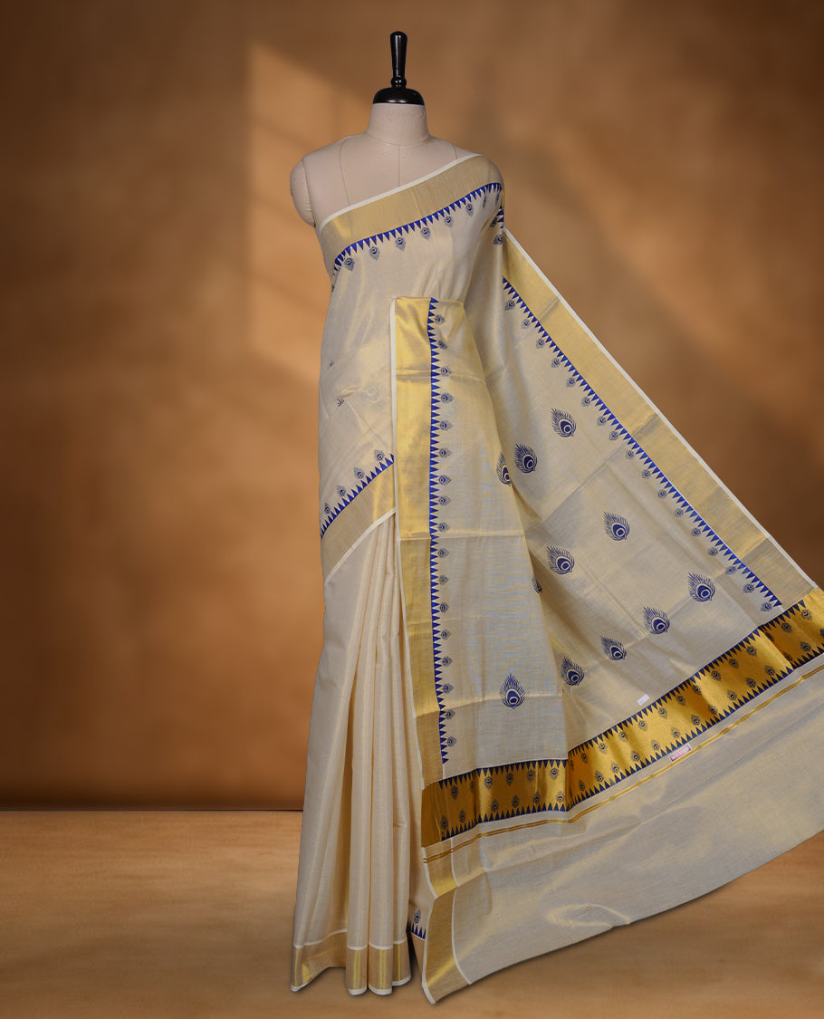 Off-white colour tissue Kerala saree with a classic gold kasavu border, highlighted by royal blue peacock motifs across the body and pallu, and paired with a matching blouse.