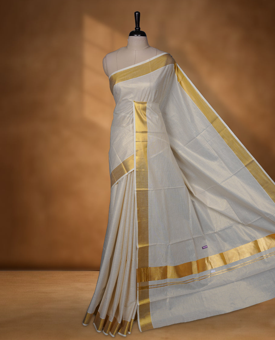 Elegant off-white colour cotton Kerala saree, highlighted with a classic gold kasavu border and subtle woven checks across the body. Finished with a clean, traditional pallu with a coordinating blouse.