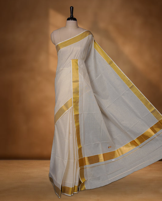 Off-white colour cotton Kerala saree with a subtle self-woven texture, finished with a traditional gold kasavu border across the body and pallu, paired with a matching blouse.