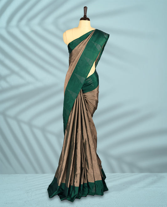 Taupe colour semi silk saree adorned with minimal geometric weave detailing, enhanced by a deep emerald green border, comes with a matching blouse.