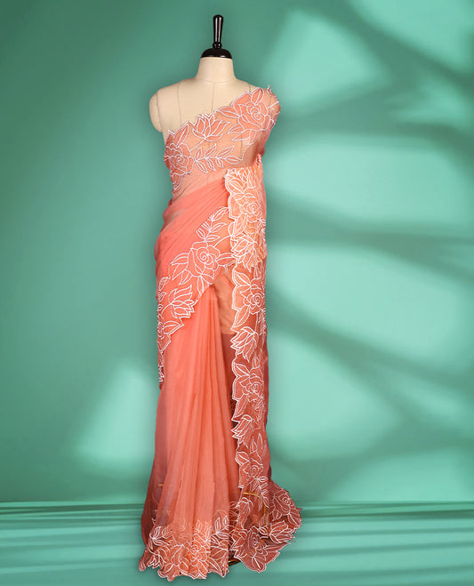 Peach colour net organza exclusive designer saree featuring a plain body and a beautifully adorned border with applique and thread embroidery work, complemented by a rich pallu and paired with a matching blouse