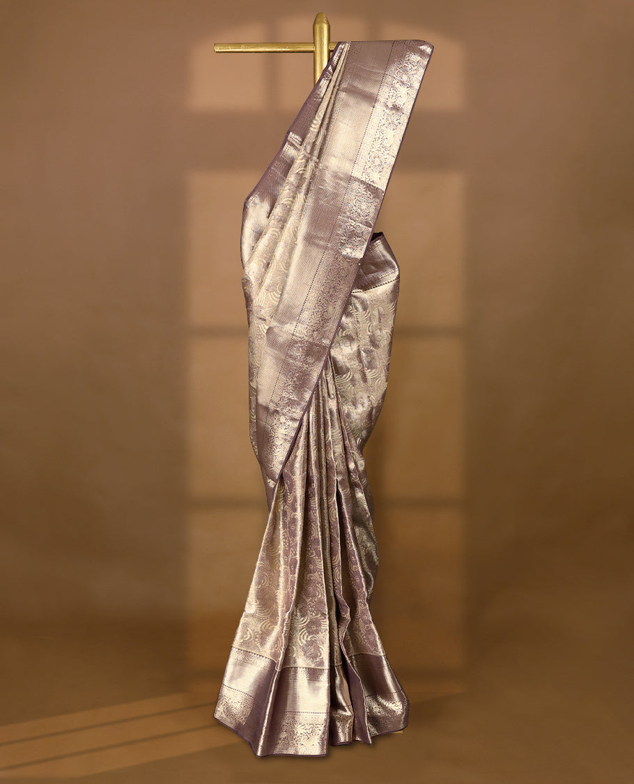 Pastel brown Colour Kancheepuram tissue silk saree adorned with intricate silver and pastel brown Zari floral motifs on the body, gracefully complemented by a traditional mango and floral design border, and paired with a matching blouse.