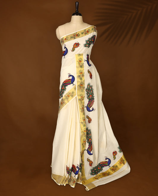 Elegant off white colour cotton Kerala saree with vibrant hand-painted peacock and feather motifs, accented by a floral printed golden border and pallu, paired with a matching blouse for a festive, graceful appeal.